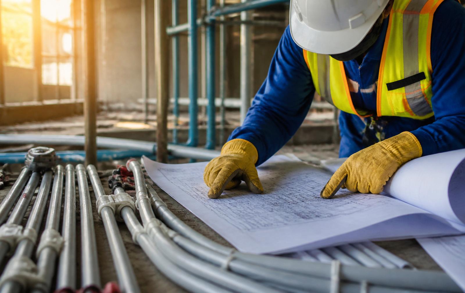 Engenheiro civil analisando projetos elétricos ao lado de eletrodutos de PVC em canteiro de obras